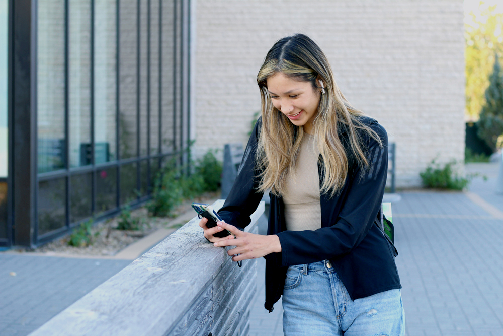 a young women looks at her phone outisde Marpeck Commons